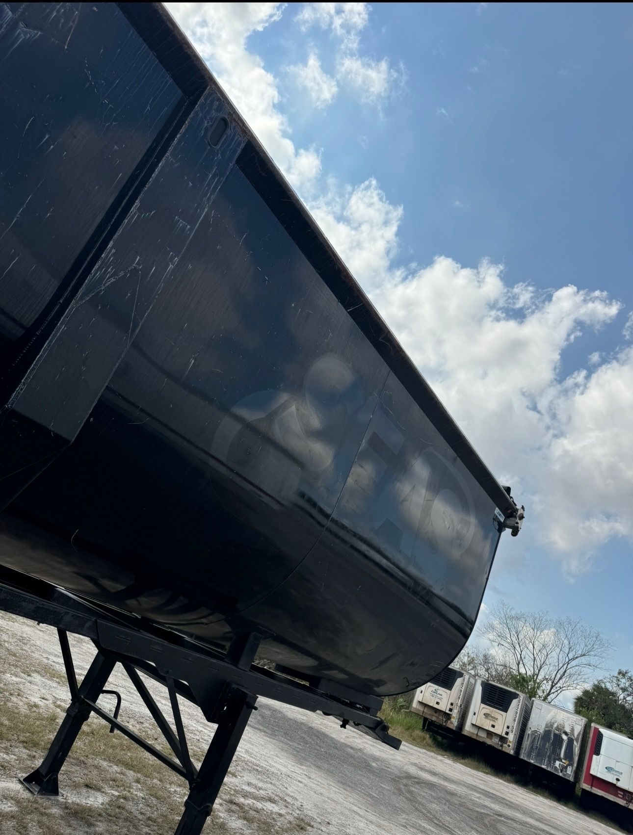 The same black dump trailer after logo and lettering removal, showing a clean gloss panel